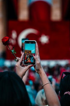 A person records a vibrant Turkish celebration in Ankara, holding a red rose.